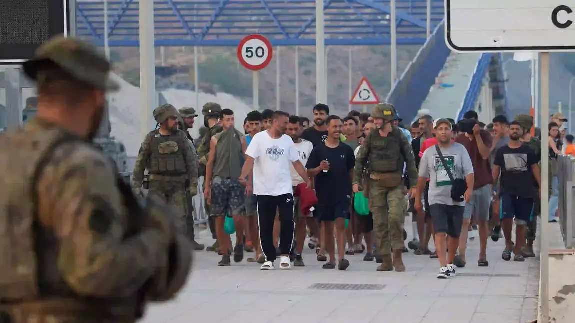 Dikawal tentara Spanyol, para imigran tersenyum menuju penyeberangan untuk kembali ke Maroko dari wilayah otonom Spanyol di Ceuta pada Sabtu, 1 Agustus 2026. (Foto AP/Antonio Sempere) Ceuta
